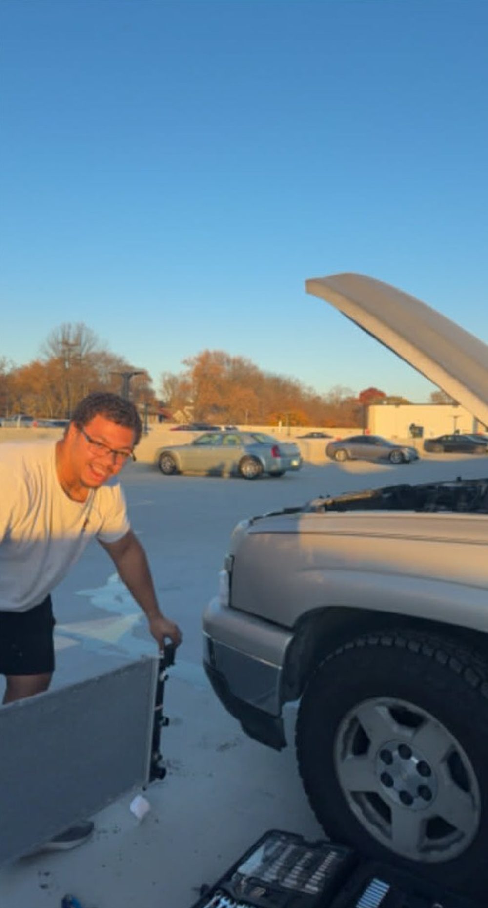 Jayden Lavespere holding the radiator he removed from a Chevrolet Silverado during an on-site repair in a parking deck